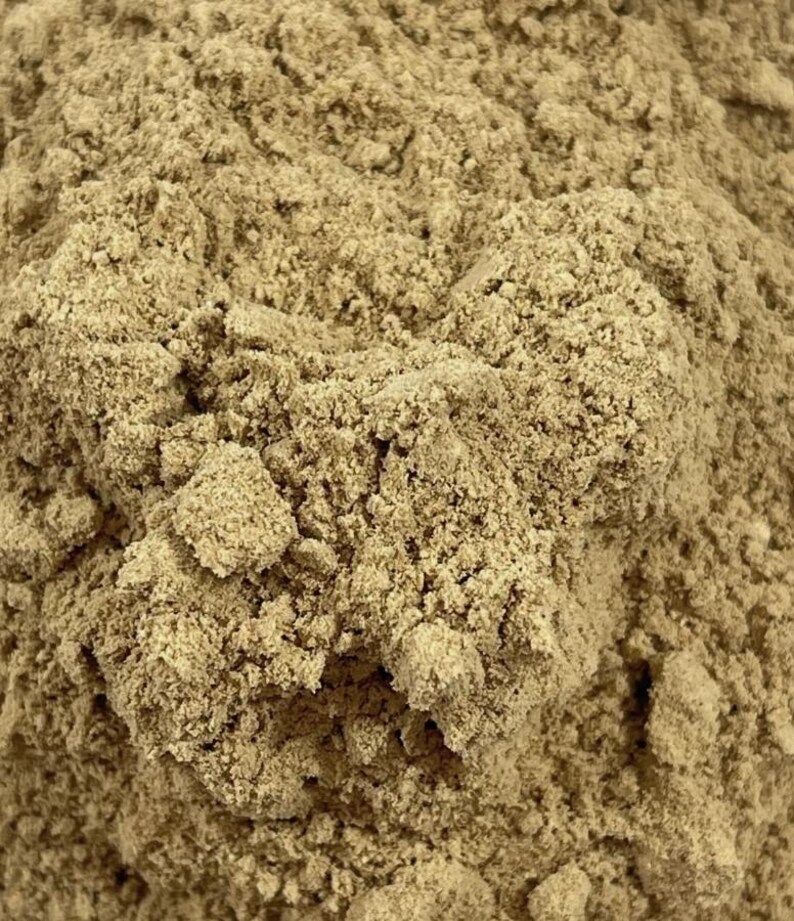 May include: A close-up view of a fine, dry, light brown powder with a granular and clumpy texture. The substance appears as a dense, uneven pile of small particles, showing variations in tone from tan to beige throughout the surface.