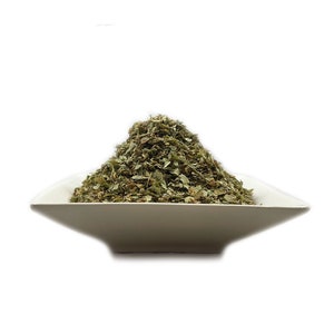 May include: A white ceramic bowl filled with a pile of dried green herbs.