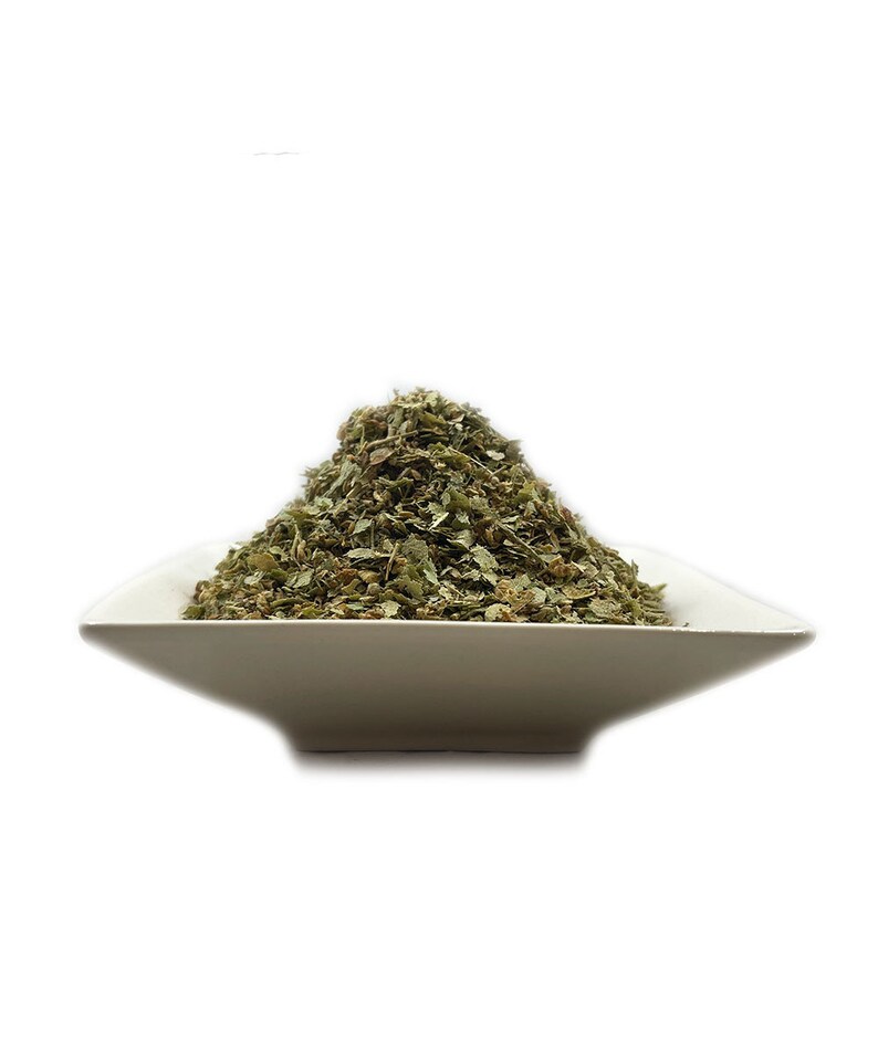 May include: A white ceramic bowl filled with a pile of dried green herbs.