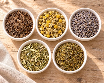 May include: Five white ceramic bowls filled with dried botanical ingredients. The bowls contain dark brown bark pieces, yellow chamomile flowers, purple lavender buds, a green herbal blend with stems, and a finely ground green herbal mixture.