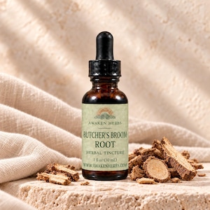 Puede incluir: Un frasco cuentagotas de vidrio ámbar con tintura de raíz de rusco. La etiqueta muestra el texto AWAKEN HERBS, BUTCHER'S BROOM ROOT, HERBAL TINCTURE, 1 fl oz (30 ml) y la dirección del sitio web www.awakenherbs.com.