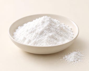 May include: A small, round, off-white ceramic bowl filled with a mound of fine, bright white powder. A small, separate pile of the same white powder is positioned to the lower right of the bowl, showcasing the texture and consistency of the substance.