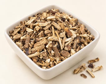 May include: A square white bowl filled with dried, chopped brown and tan root pieces. The roots have a fibrous, woody texture with varying shades of dark brown bark and lighter beige interiors. A few loose root fragments lie outside the bowl.