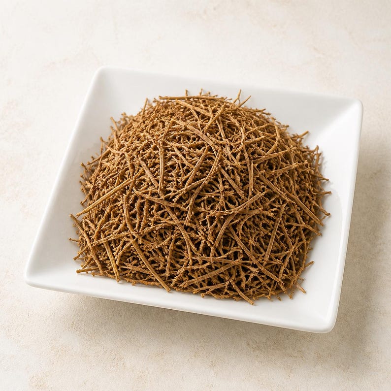 May include: A mound of dried, thin, brown herbal stems piled in a white square bowl. The stems are textured, woody, and appear brittle, forming an intricate, tangled heap that fills the center of the bowl with a uniform, earthy brown color.