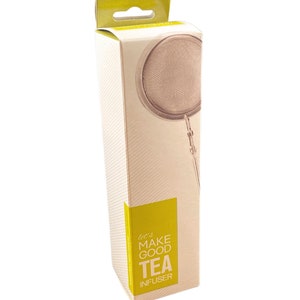 Puede incluir: Una caja de cartón amarilla y blanca con un infusor de té dorado en su interior. La caja tiene el texto "let's make good tea infuser".