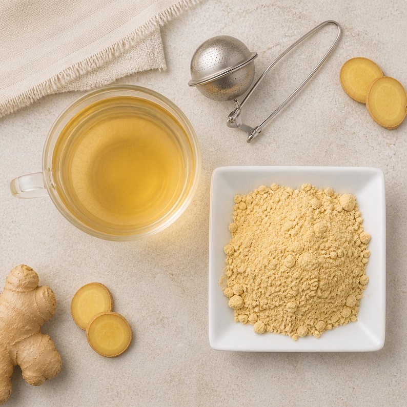 May include: A clear glass mug filled with light yellow ginger tea, a metal tea infuser, a white square bowl containing light yellow ginger powder, a whole ginger root, and several thin, round slices of fresh ginger root arranged together.