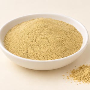 Peut inclure: Un bol en céramique blanche rempli d'un tas de poudre fine beige clair. La texture de la poudre semble uniforme et sèche, avec un petit tas séparé de la même substance beige clair reposant à l'extérieur du bol sur la surface.