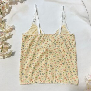 May include: A yellow tank top with a white floral print and white straps. The tank top has a scalloped hem.
