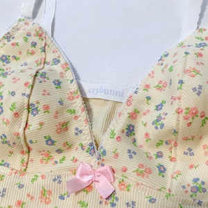 May include: A yellow floral print tank top with a pink bow and the text "crybunni" on the front.