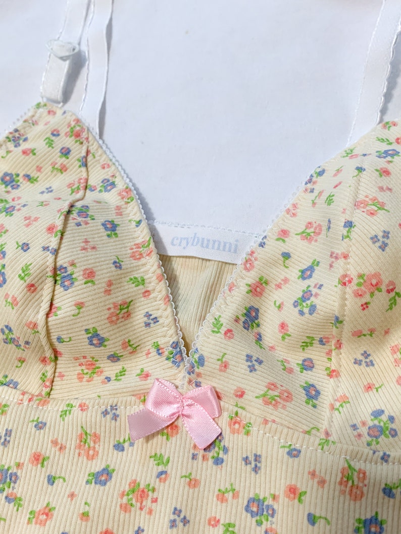 May include: A yellow floral print tank top with a pink bow and the text "crybunni" on the front.