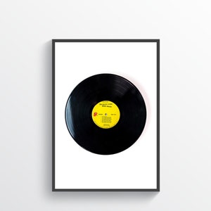 May include: Framed print of a black vinyl record with a yellow label. The label features the text "The Rolling Stones Sticky Fingers" and a red tongue logo. The record is centered on a white background within a black frame.