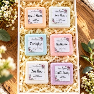 May include: A white gift box containing six square shower steamers in orange, light blue, pink, purple, and two shades of white. Each steamer features a label with the Trove Organics logo, a scent name, and a net weight of 1 oz.