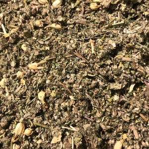 May include: Close-up of a mixture of dried herbs and flowers, including green leafy herbs, small white flower petals, and light brown pieces of dried fruit.