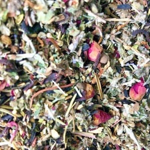 May include: A close-up of a blend of dried herbs and flowers, including green leaves, brown pieces, and pink flower petals.