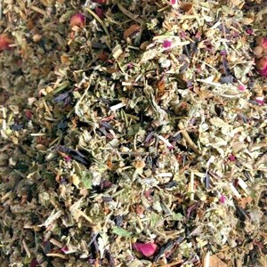 May include: Close-up of a mix of dried herbs and flowers. The blend features various shades of green, brown, and purple, with visible pieces of dried rose petals. The texture appears coarse and natural, suggesting a herbal product.