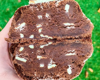 Puede incluir: Una galleta de chocolate con relleno de menta, partida por la mitad para mostrar el interior. La galleta está cubierta con una ligera capa de azúcar en polvo.