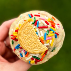Puede incluir: Primer plano de una bola de masa para galletas cubierta de chispas de colores con una galleta Oreo de chocolate en la parte superior.