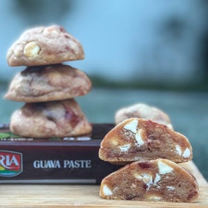 May include: A stack of four cookies with a light brown exterior and visible white chunks. The cookies are stacked on top of each other. The bottom of the image shows a box of guava paste.
