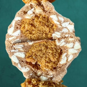 May include: A close-up of a split cookie with a white chocolate and peanut butter filling. The cookie is a light brown color and has a crispy texture.