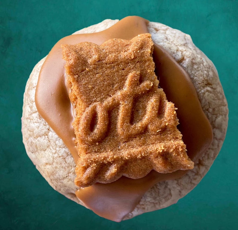 May include: A close-up of a cookie topped with caramel and a speculoos cookie. The speculoos cookie has a traditional design.