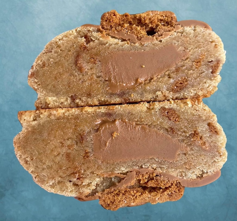 May include: A close-up of a split cookie with a chocolate filling. The cookie is light brown and has a slightly crispy texture. The filling is a rich, dark chocolate.