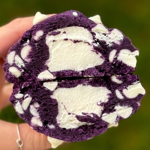 Può includere: Un biscotto viola con gocce di cioccolato bianco, spezzato a metà per rivelare un ripieno di cioccolato bianco.