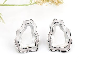 May include: A pair of silver earrings with a unique, organic shape. The earrings are made of two overlapping layers of metal, creating a textured and modern look.