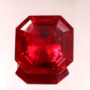 May include: A vibrant, deep red gemstone with an octagonal step-cut shape. The stone features precise geometric facets that create internal light reflections and a clear, transparent appearance with a polished surface and sharp, defined edges.
