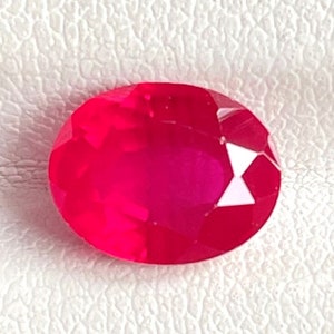 Könnte beinhalten: Ein leuchtender, oval geschliffener Edelstein in einer tiefen, gesättigten roten Farbe mit zahlreichen dreieckigen Facetten auf der Oberfläche. Der Stein weist eine hohe Klarheit und Lichtreflexion auf und zeigt ein brillant poliertes Finish.