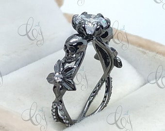 May include: Black engagement ring with a large clear stone surrounded by a skull and floral design.