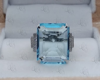 May include: A square-shaped aquamarine ring with a silver band and small diamonds on the sides. The ring is in a light brown velvet box.