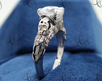May include: A silver engagement ring with a large, clear, round-cut diamond. The band is decorated with a skull and floral details.