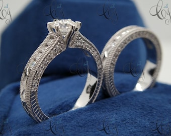 May include: A pair of silver wedding bands with a large, clear, round diamond in the center of the engagement ring. The rings are set in a blue velvet box.