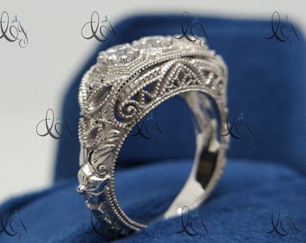 May include: A silver engagement ring with a filigree design and three clear gemstones. The ring is set on a blue velvet background.
