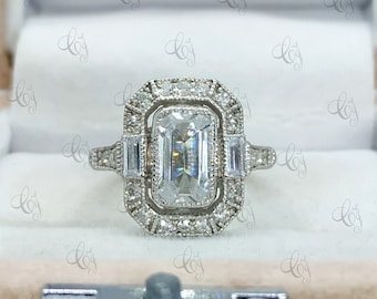 May include: A silver engagement ring with a large, clear emerald-cut center stone surrounded by a double halo of smaller diamonds. The ring has a delicate, vintage-inspired design.