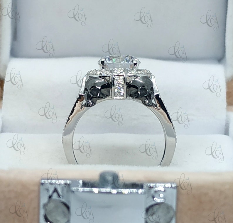 May include: A silver engagement ring with a large, round, clear center stone surrounded by smaller stones. The band is decorated with two skull-shaped designs.