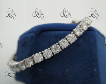 May include: A silver tennis bracelet with a row of round, clear stones. The bracelet is on a blue velvet background.