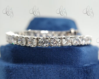 May include: A silver eternity band with a row of round, clear, sparkling stones.