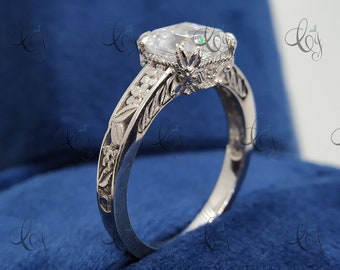 May include: A silver engagement ring with a large, clear, round-cut gemstone. The band is decorated with intricate floral designs.
