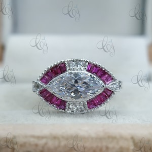 Op de afbeelding: Een zilveren ring met een grote marquise-vormige diamant omringd door een halo van kleinere diamanten en roze baguette-vormige edelstenen.