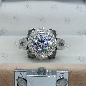 May include: A silver engagement ring with a large, round, clear center stone surrounded by a halo of smaller stones. The ring has a double band with small stones set into the band.