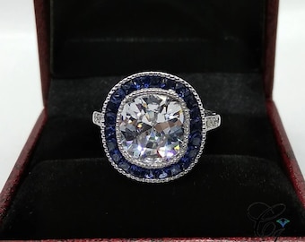 May include: A silver ring with a large, cushion-cut, clear gemstone surrounded by a halo of smaller, blue gemstones.