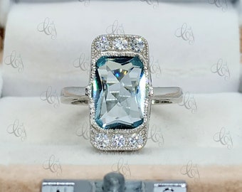 May include: A silver ring with a large, rectangular, light blue aquamarine gemstone surrounded by a halo of smaller, clear diamonds.