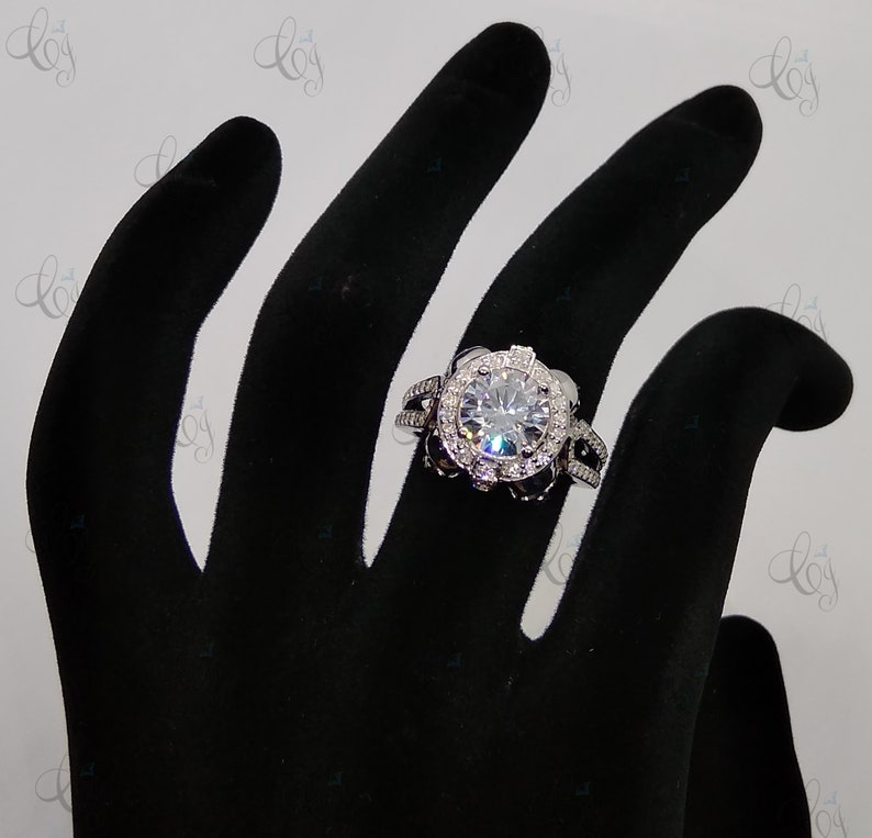 May include: A silver ring with a large, round, clear stone surrounded by smaller stones. The ring is on a black hand model.