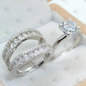 May include: A set of two silver rings with a double band design. The rings are set with small, clear stones. The rings are in a white box.