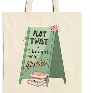 May include: Cream-coloured tote bag featuring a green sign with the text "PLOT TWIST: I bought MORE Books." The sign has a stack of books and a pink flower. The bag is made of a light canvas material, ideal for carrying books.