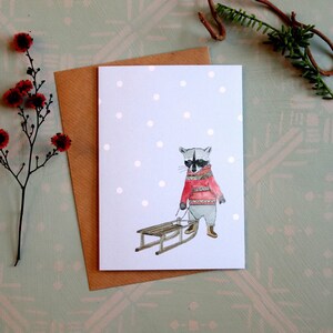 Tarjeta de felicitación "Mapache y Trineo". Horario de invierno. Navidad. Felices vacaciones. Tarjeta de Navidad. Trineo. Suéter navideño.