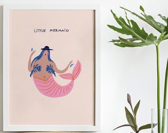 May include: A framed art print featuring a whimsical illustration of a mermaid with blue hair, a black hat, and a pink tail. The words "Little Mermaid" are written above the mermaid. The artwork is set against a light pink background.