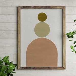 Op de afbeelding: Een ingelijste abstracte kunstprint met drie overlappende cirkels in tinten bruin, beige en perzik. De cirkels zijn verticaal gerangschikt, met de kleinste cirkel bovenaan en de grootste cirkel onderaan.