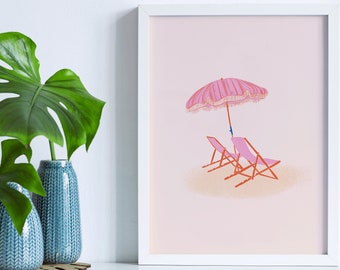 May include: A framed art print featuring a beach scene with a pink striped umbrella and two pink lounge chairs on a sandy beach. The artwork is in a white frame and is displayed next to two blue vases with green leaves.